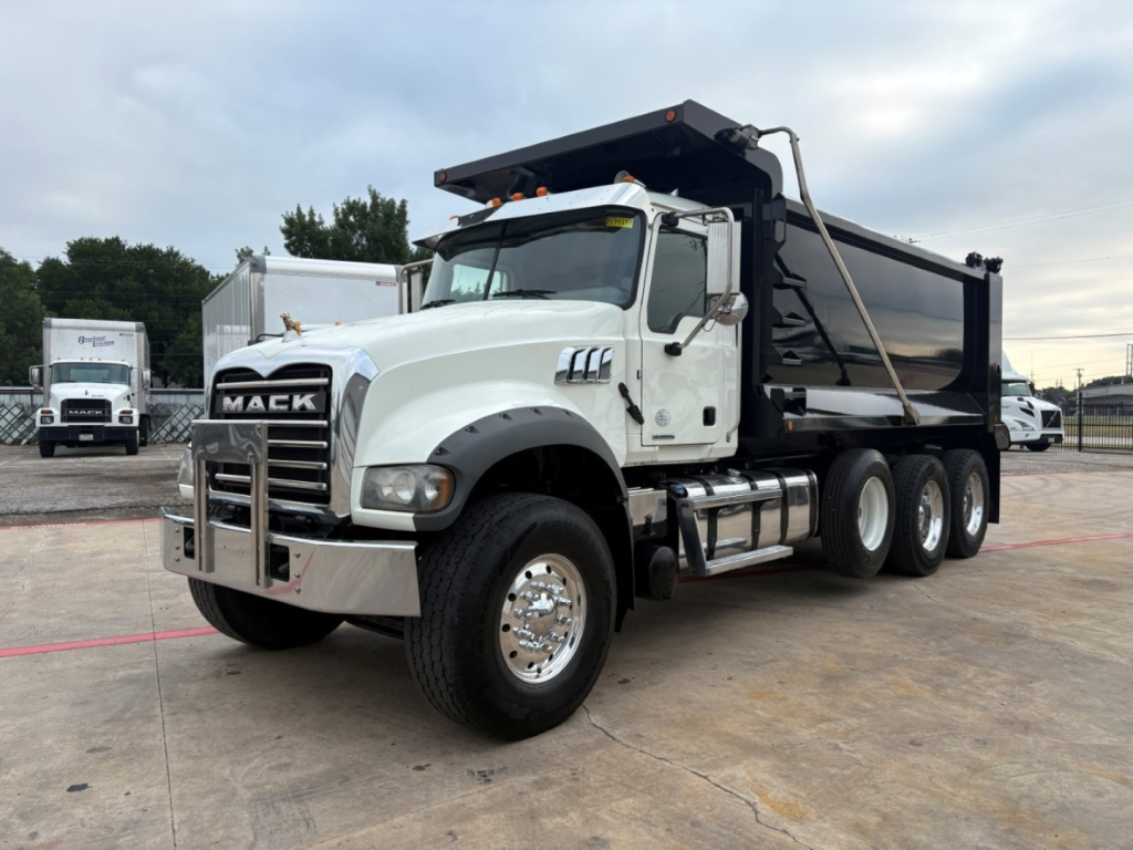 Mack GR64F dump truck side view showing large black dump bed, chrome bumper, and six-wheel axle; white cab with Mack grille