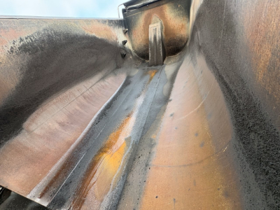 Dump truck bed interior showing metal ribs and worn coating with rust tones and a central drainage channel.