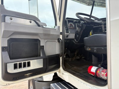 Cab interior of a 2020 Mack GR64F dump truck showing open driver door, steering wheel, dashboard gauges, and a mounted fire extinguisher on the floor near the seat.