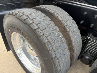 Dual rear steer tires on a Mack GR64F dump truck, showing tread pattern, chrome wheel, and suspension components.