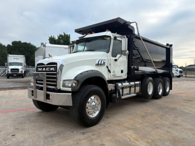 Mack GR64F dump truck side view showing large black dump bed, chrome bumper, and six-wheel axle; white cab with Mack grille