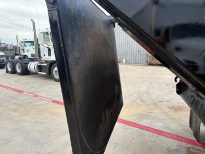 Dump truck bed corner with hydraulic lift, black metal surface, some dirt and scuff marks visible.