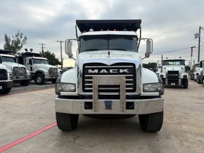 Mack GR64F dump truck front view showing large chrome bumper, grille with MACK emblem, dual headlights, and elevated dump bed in background.