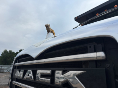 Grille of a 2020 Mack GR64F dump truck showing MACk letters on the grille and hood ornament in the foreground.