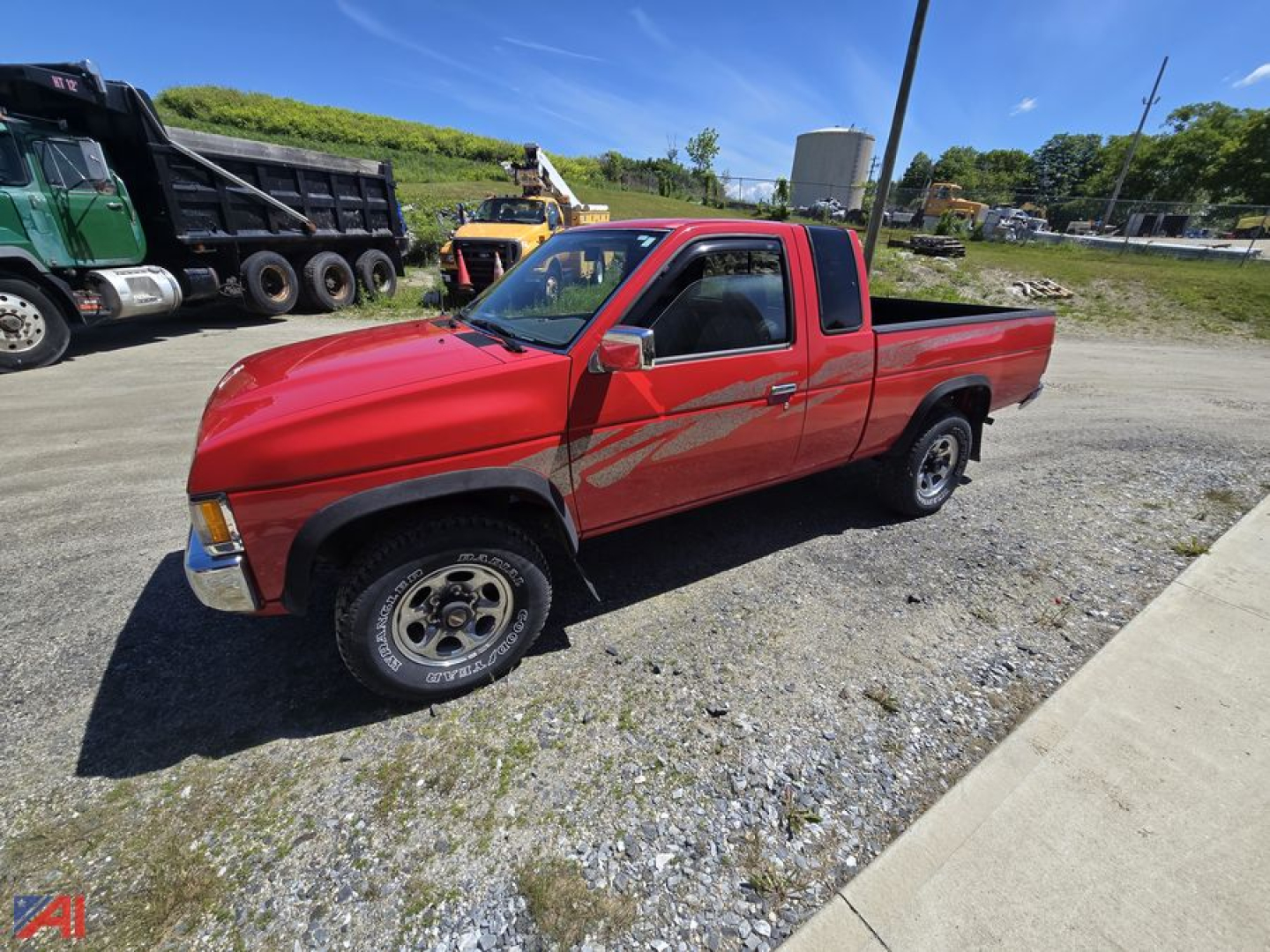 Red 1995 Nissan pickup truck in a used lot, extended cab with a long bed, black wheels, on a gravel surface.