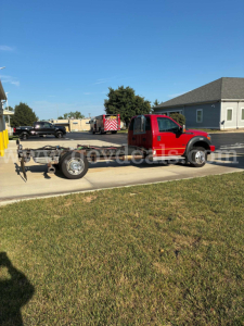 Ford F-550 cab and chassis in red with exposed chassis and rear wheels, side view.