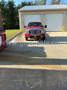 Ford F-550 cab and chassis front view with red exterior, dual front lights, large bumper, and white garage doors in background.
