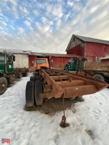 Tilt frame truck chassis on a snowy lot with rusted frame and hooklift components visible.