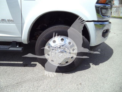 Front wheel and fender of white Ram pickup showing steel wheel and tire, with Ram badge and RAM script on side.