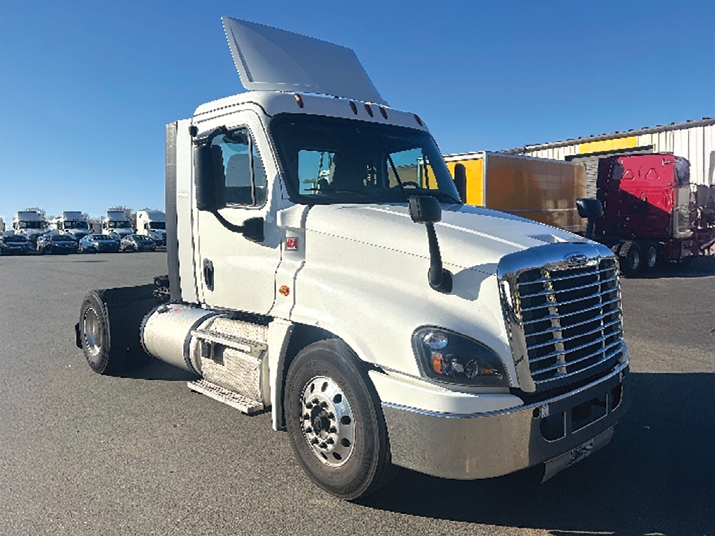Truck cab and hood of a white 2019 Freightliner Cascadia125 daycab, raised sleeper air deflector, large chrome grille, side mirrors, dual fuel tanks, exposed chassis