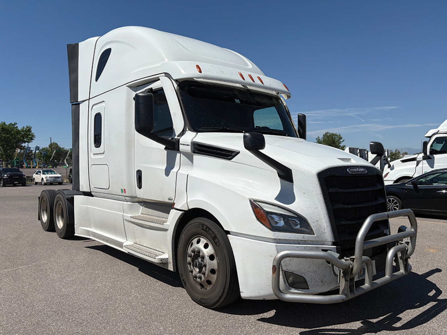 Truck cabin view of a white 2023 Freightliner Cascadia 126 conventional sleeper, front bull bar guard, side mirrors, two-axle rear with dual wheels.
