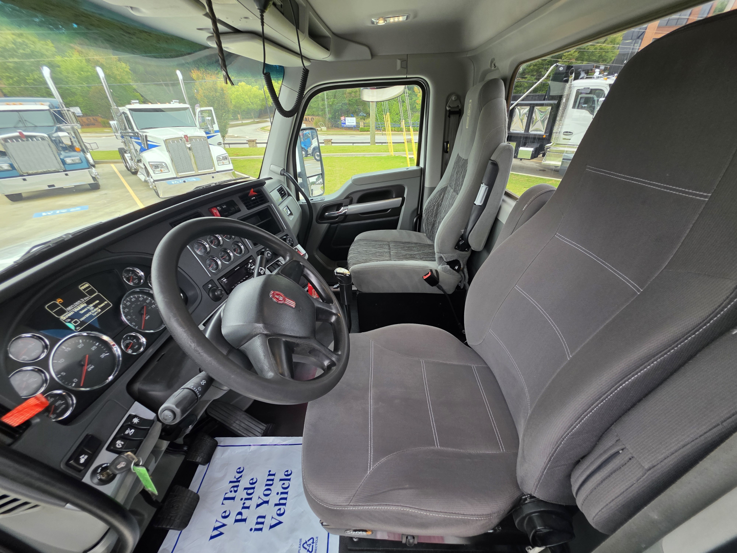 Interior of Kenworth T880 cab showing gray cloth driver and passenger seats, steering wheel, dashboard gauges, and controls.