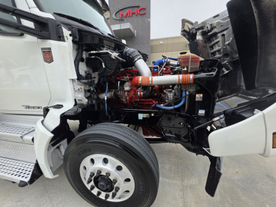 Kenworth T880 engine bay view showing front wheel, open hood, engine components, hoses, and turbo/intercooler piping under the hood.