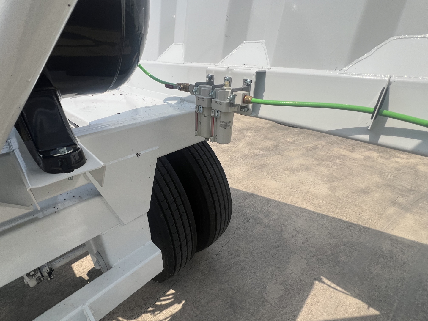 Trailer hitch area showing a green air line and a pneumatic valve connected to a white Cnsole/axle assembly with dual tires; no visible branding or text.