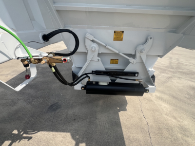 Trailer hitch area showing hydraulic lines and black hydraulic cylinder on a white dump trailer bed.