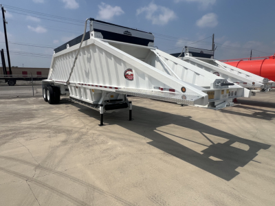 Dump trailer showing white air-ride bottom-dump with dual axles and rear hitch, label on side, and black toolbox on top; side lights visible.