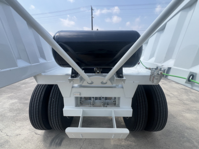 Trailer rear view showing air ride system and dual rear axles with large tires, black tank, hydraulic suspension components, and white chassis.