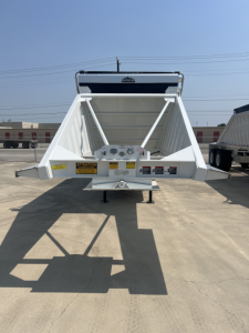 Dump trailer rear view with white air ride system, triangular frame, bumper and warning labels, rear hitch area visible.