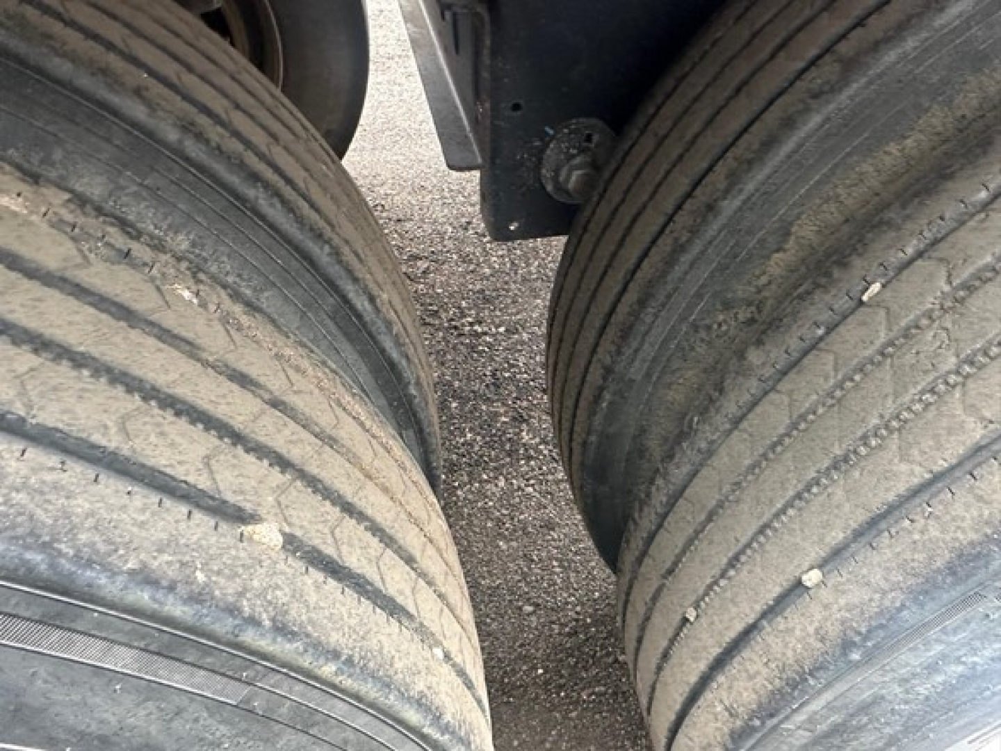 Trailer axle dual tires view with tread lines and mud, showing wheel well and suspension area.