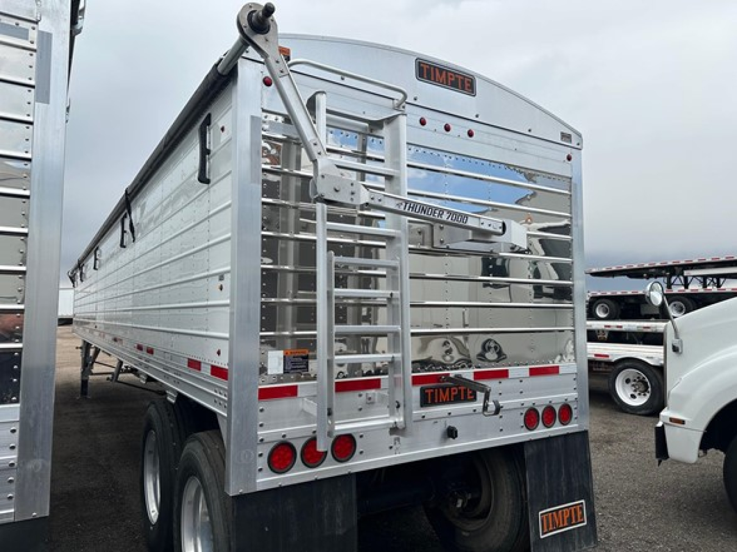 Timpte hopper trailer rear view showing Timpte branding, rear ladder, and twin axles; aluminum body with reflective striping.
