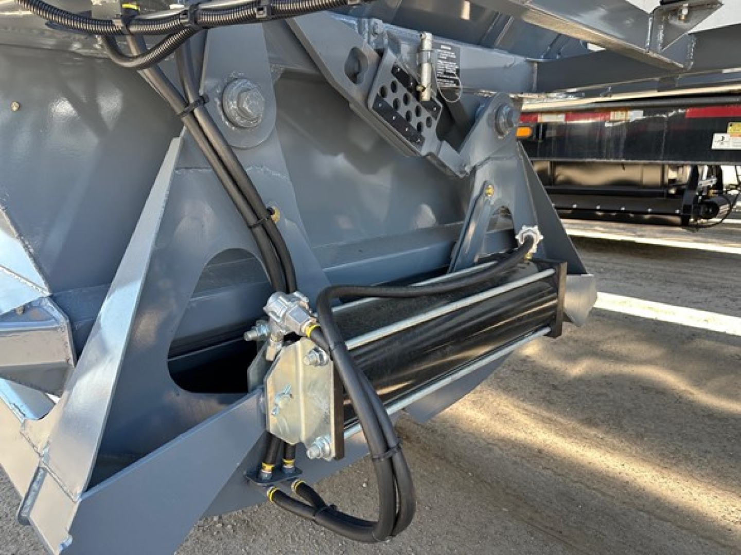 Dump trailer hitch area showing hydraulic lines and linkage on gray steel frame.