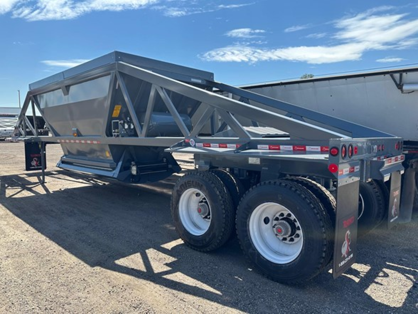 Ranco LW21-40 dump trailer on-site with tandem axles and gray chassis, side railing, and hydraulic dump bed.