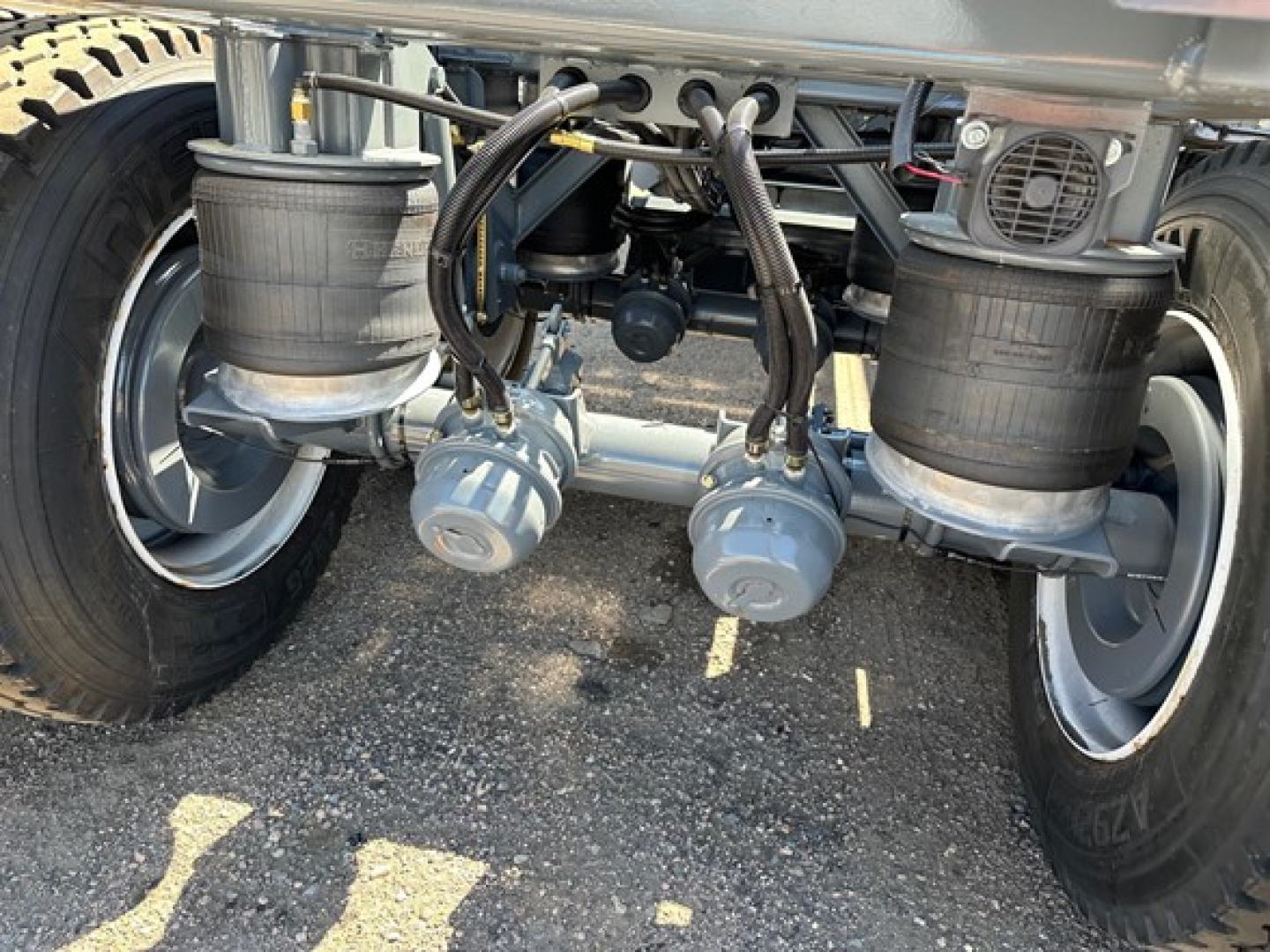 Ranco LW21-40 dump trailer undercarriage showing dual air bags, piping, and two gray pneumatic cylinders along the axle with tires on both sides.