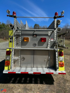 Back view of a 1989 Mack fire truck with diamond plate aluminum body, two red and orange rear warning lights, vertical ladders, compartments, and a rear bumper with reflective stripes.