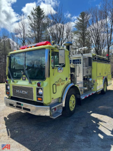 Mack fire truck in-service showing front grille, windshield, and side equipment compartments with yellow paint and red emergency lights.