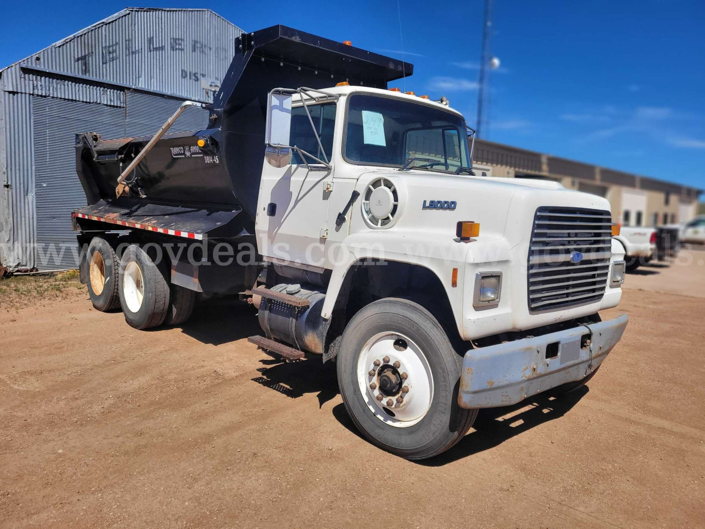 Ford LT9000 dump truck with white cab and black dump body, front grille, dual rear axles, visible VIN plate area, road grime on tires and body.