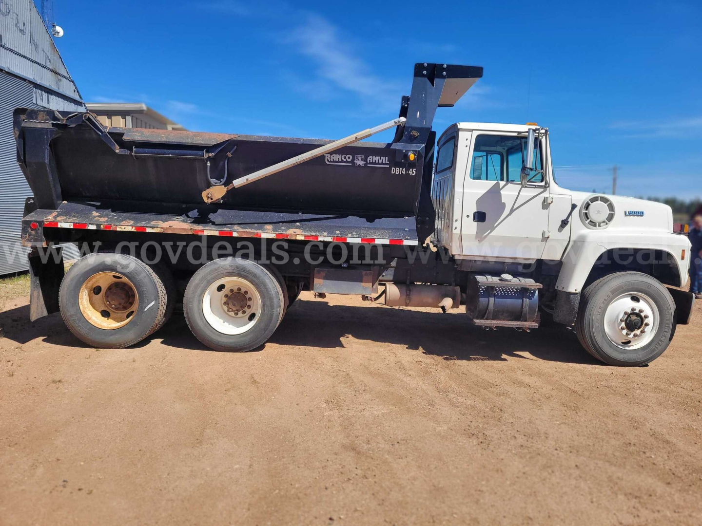 Ford LT9000 dump truck side view showing dump bed with hydraulic arm and rear wheels, white cab with black dump body.