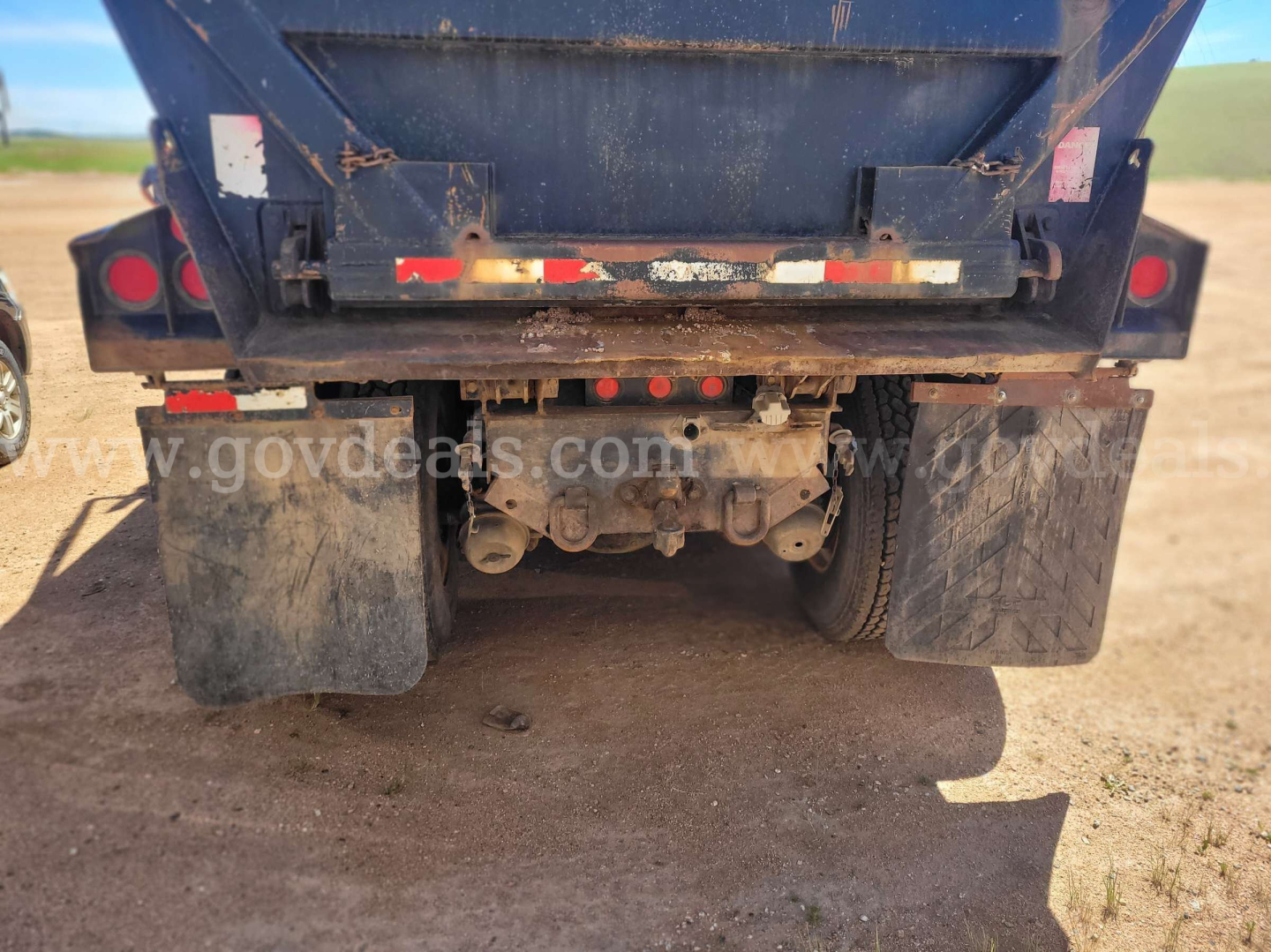 Rear view of a Ford LT9000 dump truck showing dual rear axles, mud flaps, and linkage under the dump bed.
