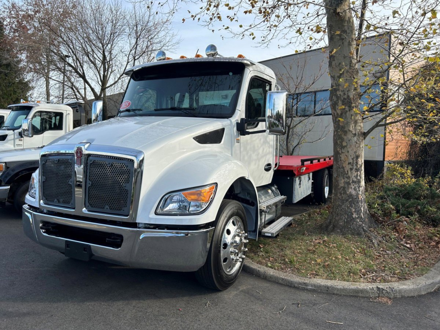 Kenworth T280 tow truck front-left view showing large chrome grille and dual mirrors with flatbed behind.
