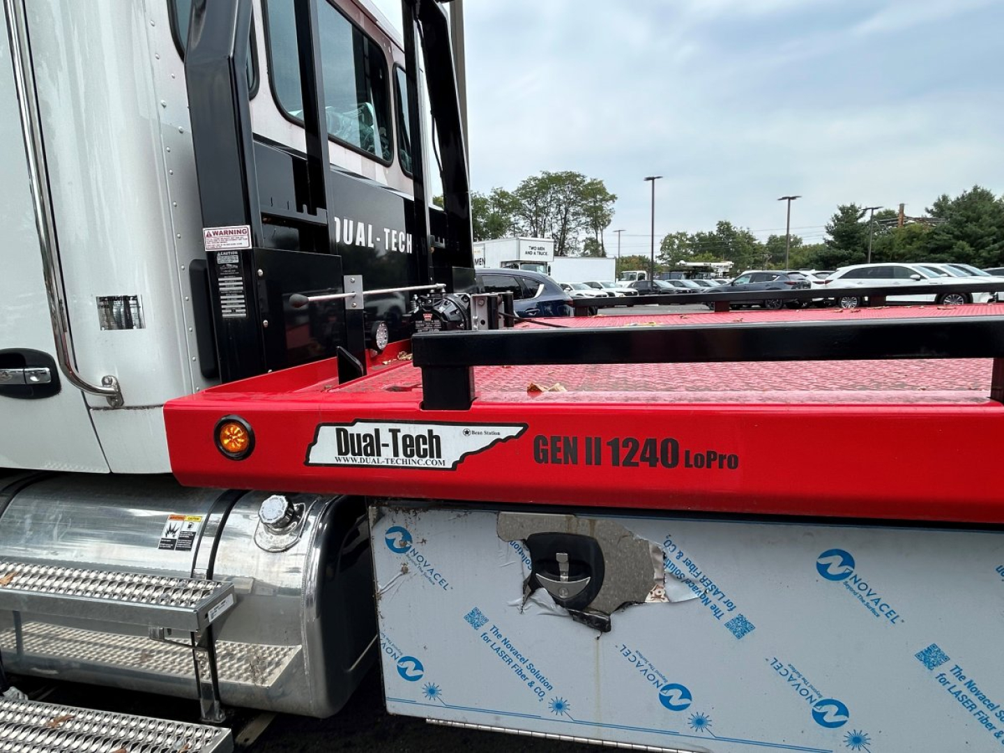 Kenworth T280 tow truck side view showing Dual-Tech GEN II 1240 Lopro red equipment carrier mounting with white cab and metal steps; visible VIN sticker area and stock number label.