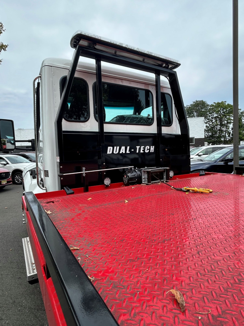 Tow truck cab rear with Dual-Tech branding on the sleeper window and a redDiamond-plate flatbed. Visible text includes DUAL-TECH on the cabin door.
