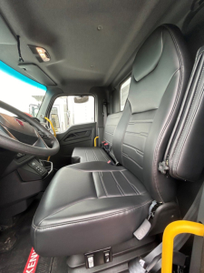 Truck cabin interior of a Kenworth T280 showing driver and passenger seats, steering wheel, dashboard, and door; black leather seats with stitching.