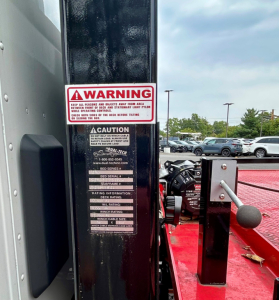 Tow truck equipment with warning label and control handle visible on a black vertical post.