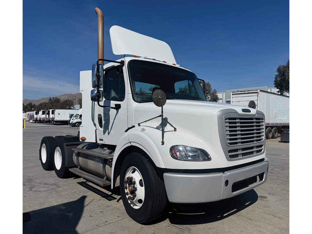 Freightliner M2 112 truck side view showing front grille, dual rear axles, exhaust stack, and cab with white paint.