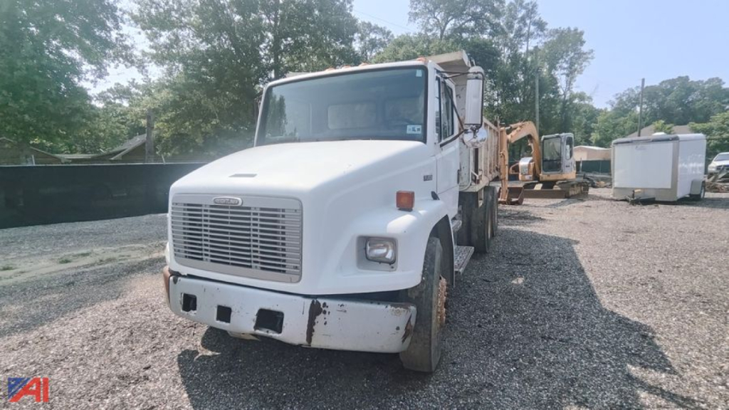Dump truck front view showing 2004 Freightliner FL80 with white cab and white front bumper; rugged front grille, rectangular headlights, and side mirrors; equipment yard background.