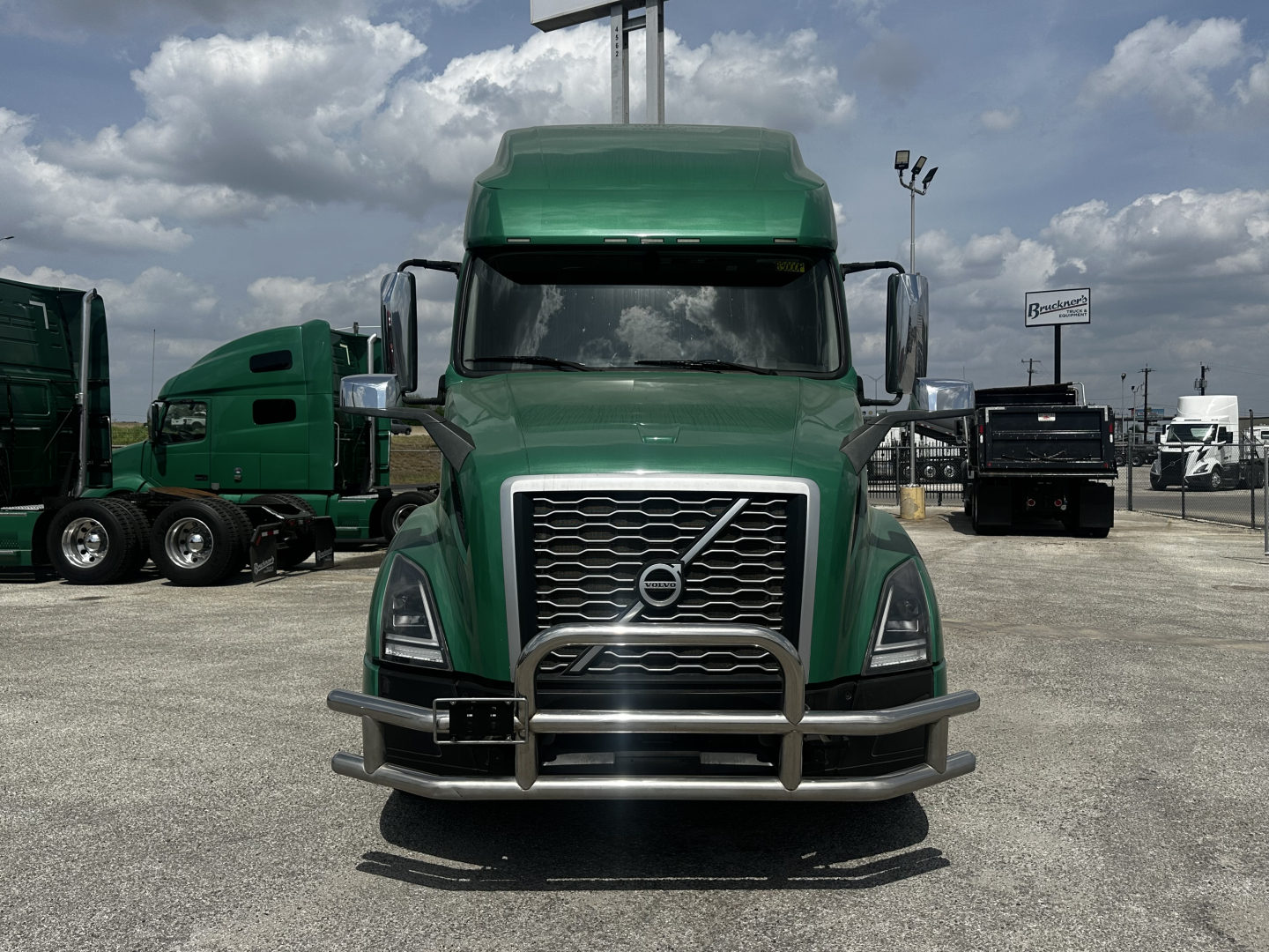 Green Volvo VNL64T760 truck front view with chrome grille, bumper, and large side mirrors.