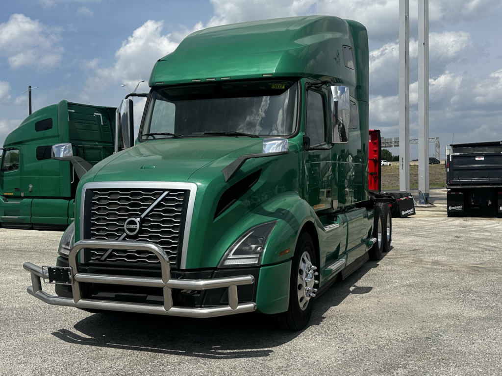 Green Volvo VNL64T760 conventional sleeper tractor profile with chrome grille guard and aerodynamic bumper, front view.