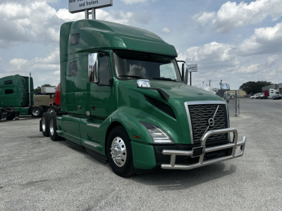Green Volvo VNL64T760 truck cab in a parking lot with chrome bumper and grille, side mirrors, and sleeper cab.