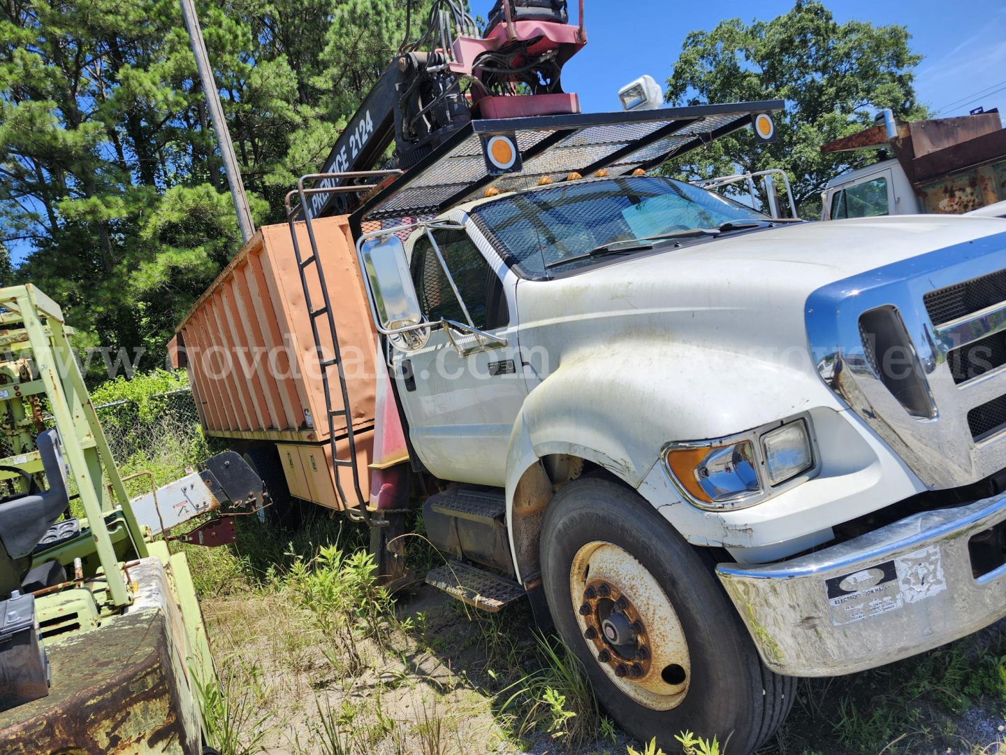 Ford F-750XL grapple truck showing front-right view with damaged fender and assets on bed; visible wheel, side mirrors, and crane equipment.