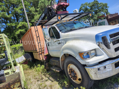 Ford F-750XL grapple truck showing front-right view with damaged fender and assets on bed; visible wheel, side mirrors, and crane equipment.
