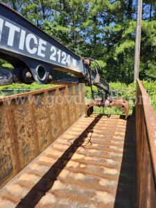 Front view of a used 2007 Ford F750XL trunk/grapple truck with rusted excavator grapple arm and open cargo bed, visible trees in the background.