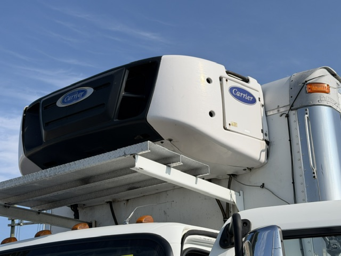 Carrier refrigeration unit mounted on Freightliner M2-106 truck cab in a refrigerated vehicle setup.