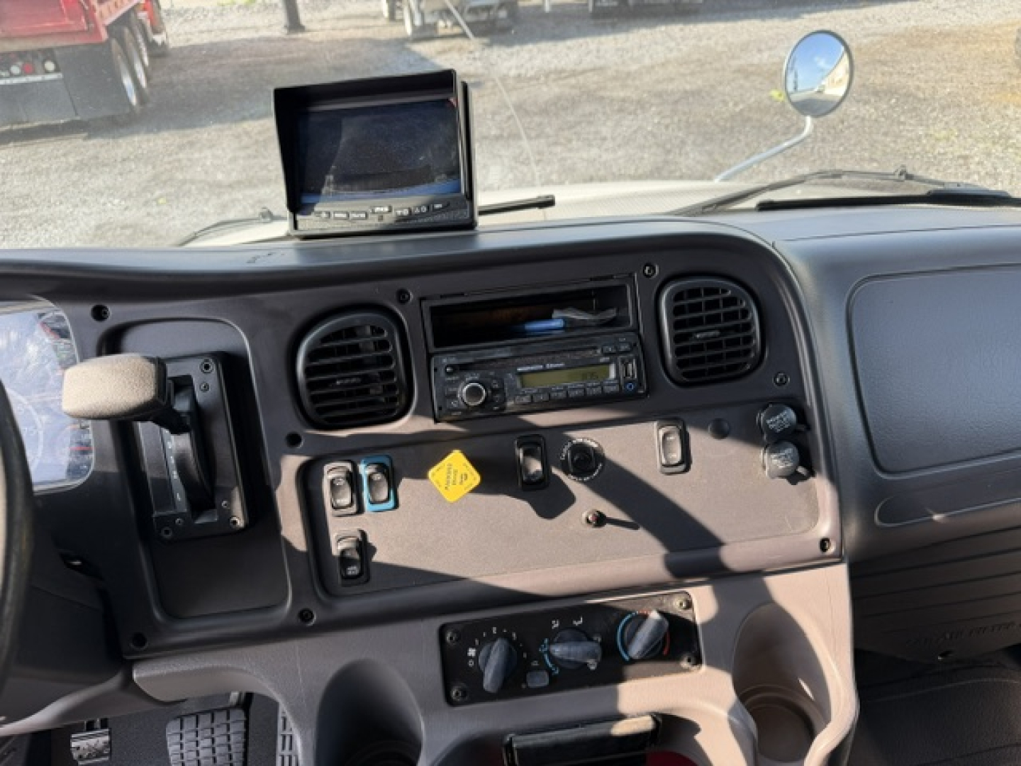 Cab interior of a 2016 Freightliner M2-106 showing dashboard, steering column, analog gauges, vents, and a mounted monitor.