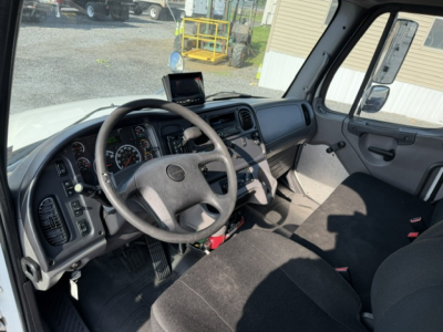 Freightliner M2-106 cab interior showing steering wheel and dashboard with overhead monitor.