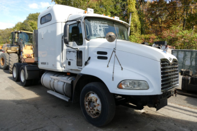 2006 Mack CXN613 conventional sleeper truck in white parked with other heavy equipment nearby, showing cab, front grille, and side fuel tanks.