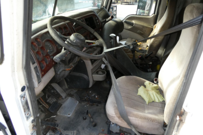Truck cab interior showing steering wheel, dashboard with circular gauges, and driver seat with seatbelt in Mack CXN613 cab.